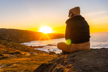 A young woman with a wool cap relaxed in winter watching the sunset on the Jaizkibel mountain in...