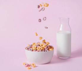 sweet colorful cornflakes rings fly in a white bowl with a bottle of milk on a pink background. Front view and copy space