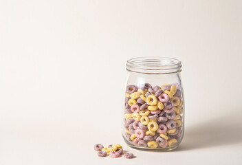 sweet colorful cornflakes rings in a glass jar on a yellow background. Front view and copy space