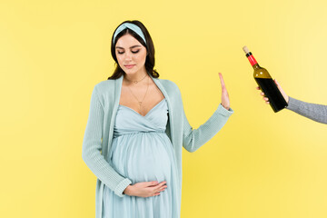 young pregnant woman refusing from red wine isolated on yellow.