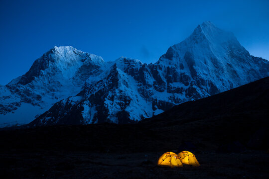 Two illuminated tents at Lobuche East basecamp with the peaks of Taboche and Cholatse in the background in Nepal's Khumbu region.