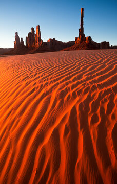 Monument Valley's Totem Pole and surrounding sandstone towers above wind swept sand dunes.