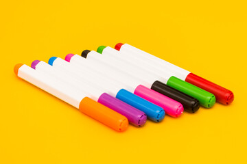 Row of multi color pen on yellow background.