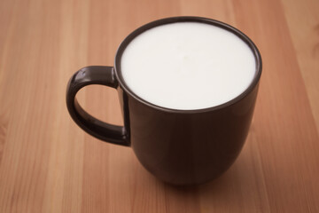 Black mug with white milk on the table. Light breakfast at home.
