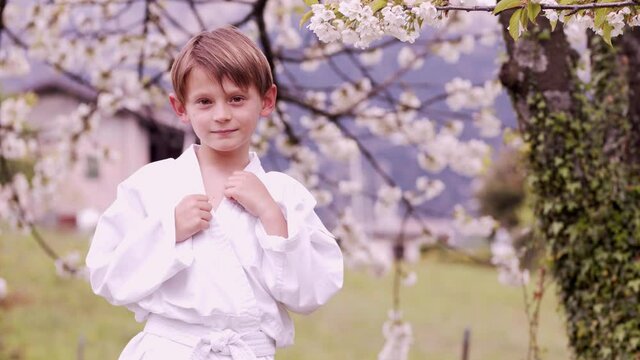 The child trains by doing karate in the open air. Football of the young karateka near the cherry tree.slowmotion