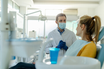 Male dentist in dental office talking with female patient and preparing for treatment.