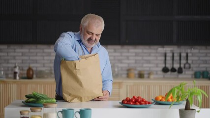 aged man is unpacking food after shopping at market at sunday morning, putting food on kitchen table at home