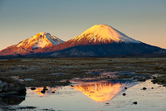 The twin volcanoes Parinacota in Chile (on right) and Pomerape in Bolivia (on left) rise above the puna to over000' above sea level during sunset.