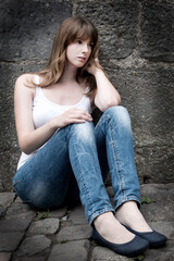 Portrait of a sad young woman looking thoughtful about troubles, she is sitting in front of a gray wall