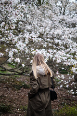 Beautiful young girl walks among the flowering trees of Magnolia in the park. Happy woman enjoys...