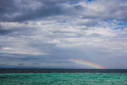 A rainbow appears on the horizon looking out from Coco Plum Island, Belize.