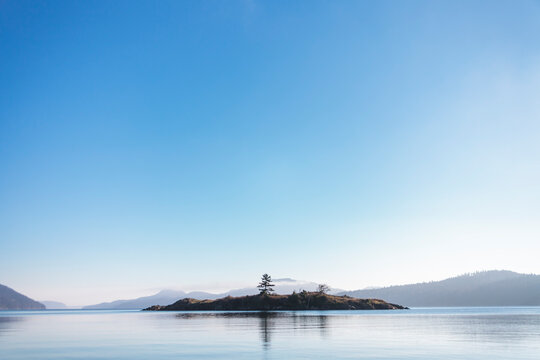 A small island sits across from East Sound on Orcas Island with calm skies and waters.