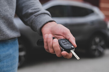 Man in front of the new car and holding keys. Salesman is carrying the car keys delivered to the customer at the showroom with a low interest offer.  Rent, credit, insurance, car purchase. Copy space