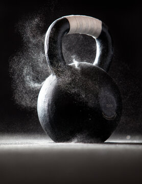Dramatic product image of a black CrossFit kettlebell with tape on the handle and chalk dust swirling off of it.