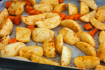 Potatoes and carrots with spices on a baking tray ready to be baked