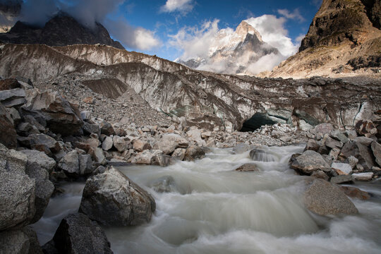 Water gushes out of the base of the Ushba Glacier with Mount Ushba, elevation 4710 M, in the background. Caucasus Mountains on the Georgian-Russia border.