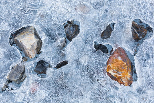 Dark rocks, absorbing more sunlight than the surrounding ice, selectively melt a layer of ice formed on the surface of a meltwater pool on Samarinbreen, Hornsund, Svalbard.