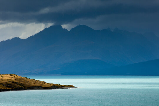 A rainstorm clears from Aoraki / Mt. Cook National Park revealing the aqua-colored glacial melt of Lake Pukaki and the rugged peaks of the Southern Alps in New Zealand's South Island.