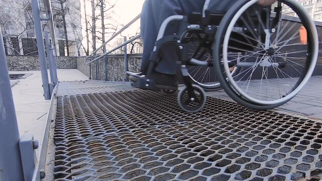 A man with disabilities moves along the street in a wheelchair, goes down the ramp