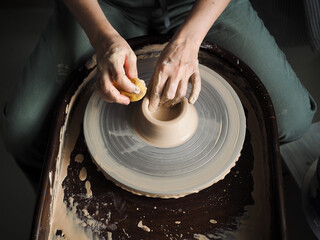 Young female master working on a potter’s wheel, creates clay dishes, view from above.
