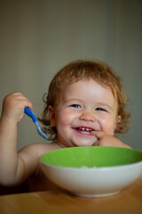 Kid baby eat soup in the kitchen with dishes and spoon. Launching child eat.