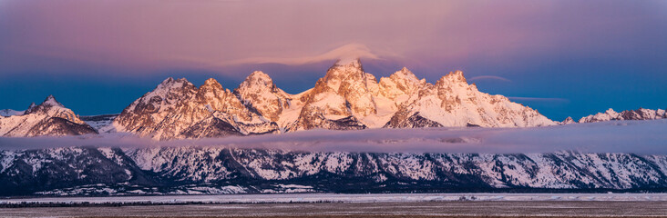 Sunrise breaks through fog to light the peaks of the Teton Mountains in Grand Teton National Park, Wyoming.