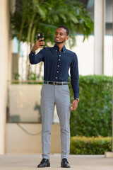 African businessman outdoors at rooftop garden using mobile phone full length shot