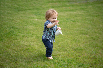 Baby standing barefoot on the green lawn.
