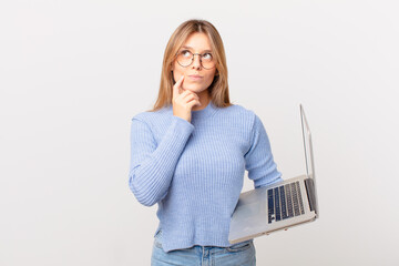 young woman with a laptop thinking, feeling doubtful and confused