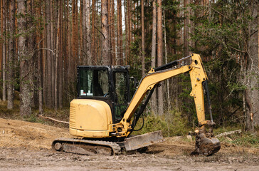 Yellow belt excavator in a pine forest. Hydraulic earthmoving harvester. Rotating operator's cab. Construction industry.