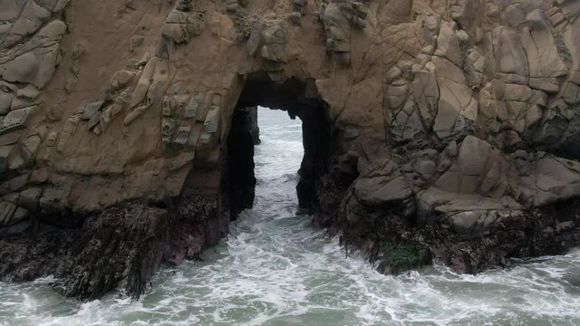 Aerial Shot Of People At Keyhole Arch On Shore, Drone Ascending Backward Over Famous Pfeiffer Beach Splashing Waves - Big Sur, California