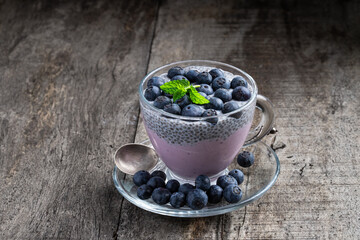 Purple blueberry yogurt with fresh berries chia seeds in glass cup on wooden table