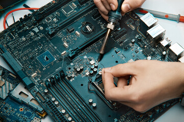 A man holds a tool for repairing electronics, manually assembling a solder circuit board.