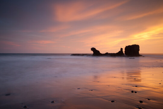 A vibrant and colorful sunset, blurred water, pebbles, and monolith at Bocanita Beach in El Tunco, El Salvador.