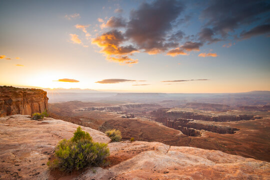 The sun peaks over the La Sal Mountains washing the canyon below in light.