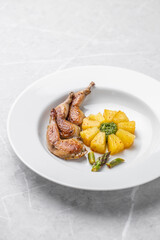 Modern restaurant dish of roasted quail legs decorated with pineapple slices. pesto and asparagus