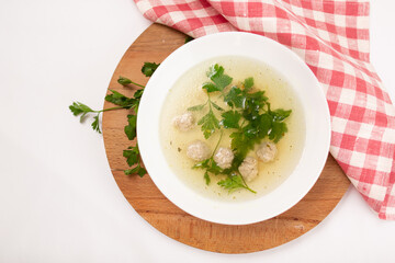 Homemade meatballs soup with vegetables in a white plate.