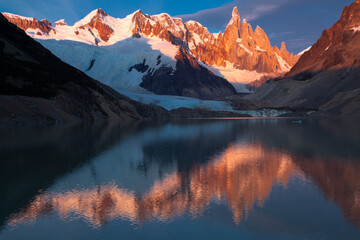 Golden mountain peak and light up with first light upon Cerro Torre and reflect in the lake below in Patagonia, Argentina.
