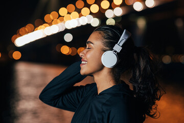 Side view of a fit woman in hooded shirt listening to music against night lights