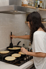 Latin woman dressed casually in the kitchen stirring eggs with cheese and heating Colombian arepas