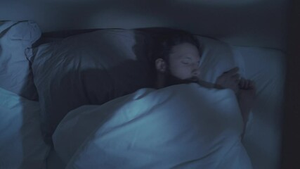 Sleep disorder. Night insomnia. Stress fatigue. Tired bored annoyed man tossing turning covering face with blanket lying in bed awake in dark bedroom with blue moonlight.