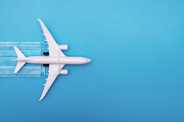 Naklejka premium A plane model with a medical mask on a blue background. Safety flight and travel during quarantine and lockdown. Safe travels concept. Opening borders