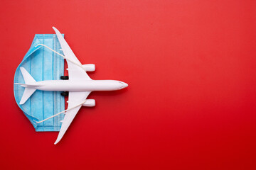 A plane model with a medical mask on a red background. Safety flight and travel during quarantine and lockdown. Safe travels concept. Opening borders