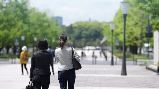 屋外で並んで歩く二人のマスク姿のビジネスウーマン