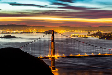 The view from above the Golden Gate Bridge at dawn with the city of San Francisco twinkling in the background
