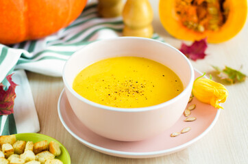Foliage leaves, flowers and creamy pumpkin soup with vegetables, seeds and croutons in a bowl, close up. Thanksgiving Day. traditional autumn dish. soft focus
