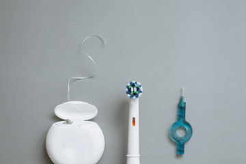 Electric toothbrush, floss and interdental brushes on a gray background. Flat lay, copyspace