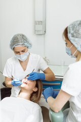 Medical treatment at the dentist office. Female dentist and assistant in dental office examining young woman with tools in dental clinic