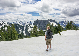Adventurous male hiker in the mountains standing in the snow looking at the landscape.