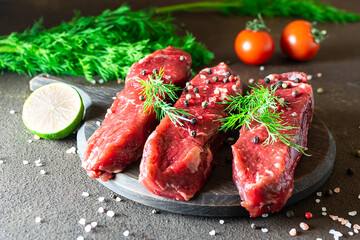 Raw beef steaks with herbs, spices and vegetables on dark kitchen table close up.